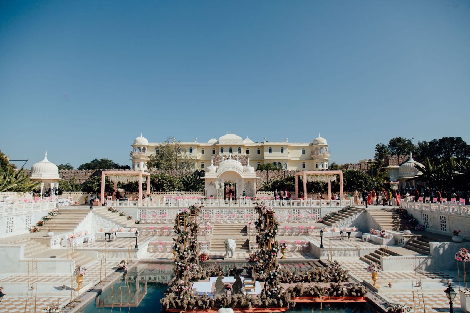 A destination wedding set up across the terraces and reflecting pool of a Rajasthan palace, chairs and mandap in place and guests beginning to gather