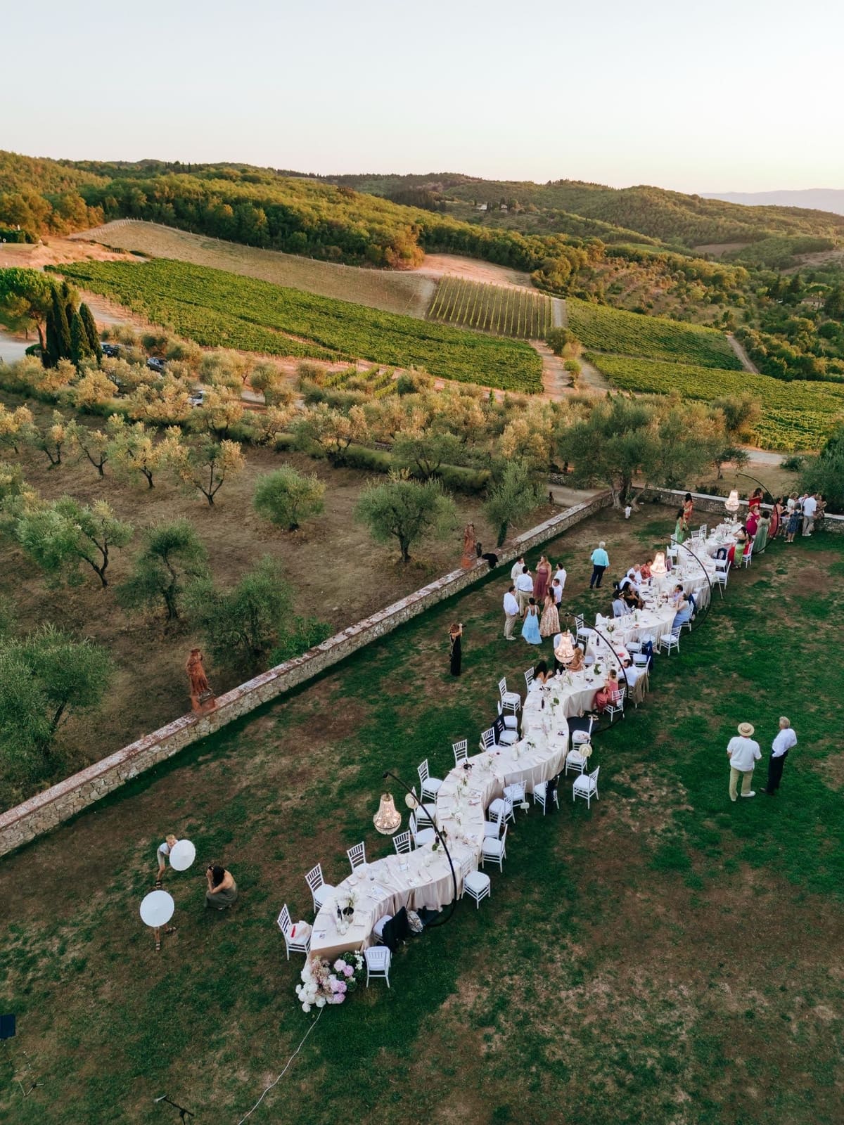 The long dinner table set for Sarah and Martin's guests on the lawn at Le Filigare, seen from above at golden hour