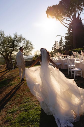 The bride crossing the lawn at golden hour, veil catching the light, guest tables set behind her